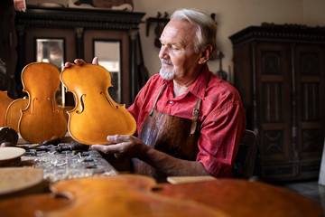 Talented and creative people. Senior carpenter building violin music instrument. Old fashioned...