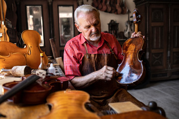 Senior carpenter craftsman polishing violin instrument in his carpenter's workshop. Creative and...