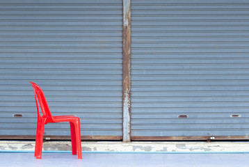A picture of a red plastic chair with additional text composition and a gray metal door backdrop.