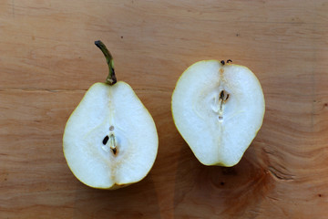 A pear cut in half lies on a wooden board.
