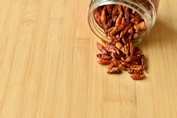Red hot chilli peppers pour down from an open jar on a wooden table