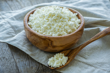 Fresh cottage cheese in a wooden bowl on a linen napkin and a wooden old background