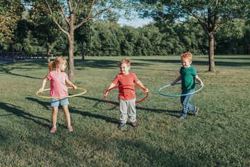 Naklejka na ściany i meble Cute smiling Caucasian preschool girl boys friends playing with hoola hoop in park outside. Kids sport activity. Lifestyle happy childhood. Summer seasonal outdoors game fun for kids children.