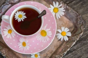 Obraz na płótnie Canvas Pink cup of tea with hearts, on a tray with chamomile flowers.