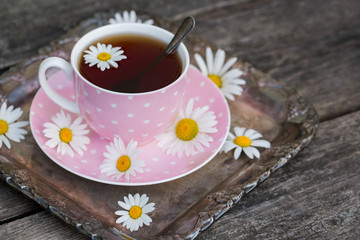 Pink cup of tea with hearts, on a tray with chamomile flowers.