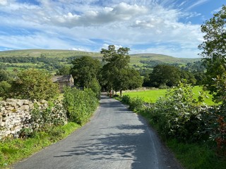 A country lane, with dry stone walls, fields, farmhouse, with trees and hills in the distance near, Aysgarth, Leyburn, UK