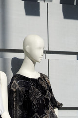 white plastic female mannequin in dark clothing through glass in a shop window on a summer day in Europe