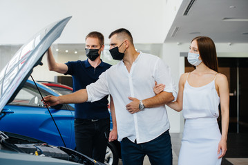 Young couple in masks selects a new vehicle and consult with a representative of the dealership in the period of the pandemic. Car sales, and life during the pandemic