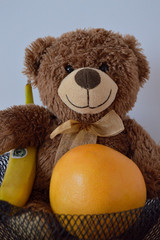 Sweet teddy bear and grapefruit width banana in black basket. - obrazy, fototapety, plakaty