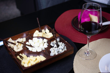 Obraz na płótnie Canvas Wine and cheese. Wooden cheese board with gouda cheeses, fresh parmesan, parmesan and gorgonzola, served with red wine on a black topped table