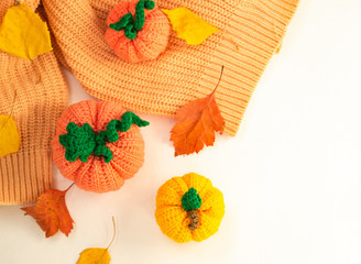 Autumn composition of three pumpkins, knitted decor of pumpkins and a sweater, and autumn leaves of orange and yellow trees on a white background, yarn and needlework, soft light. Copy of the space