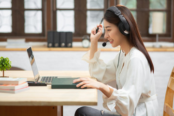 Smiling Asian young female using headset looking at laptop screen listen and learning online...