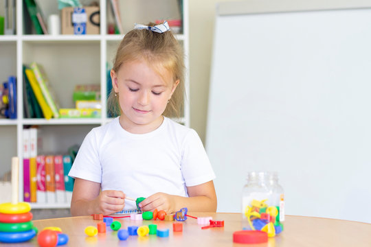 developmental and speech therapy classes with a child-girl. Speech therapy exercises and games with beads. The girl has beads in her hands