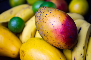Iron basket with fruits, containing banana, orange, lemon, mango and papaya on a black table.