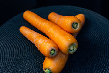 Raw carrots on a black straw background