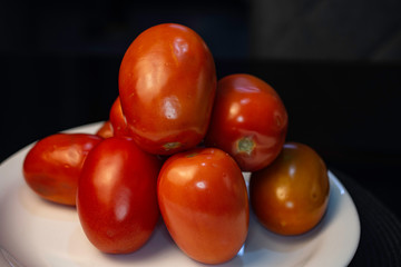 Fresh raw red tomatoes on a white plate on the black table.