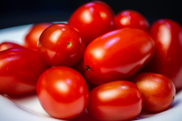 Tomate pequeno vermelho fresco cru em um prato branco sobre a mesa preta.