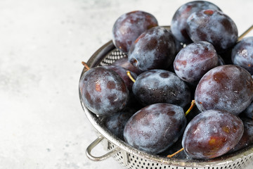 Ripe plum. Lots of plums in a metal bowl on a light background. Blue plums close-up. Healthy fruits