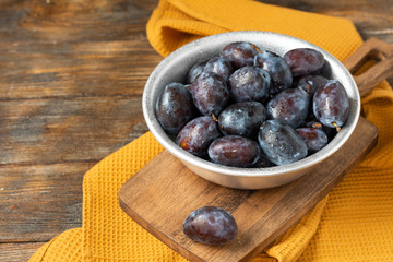 Ripe plum. Lots of plums in a metal bowl on a brown wooden table. Blue plums in a bowl close-up. Healthy fruits