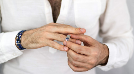 Obraz na płótnie Canvas White man's hands putting on a silver ring with a blue sapphire. Jewelry for men. Engagement ring.