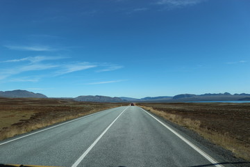 Road surrounded by countryside and with mountains and blue sky in the background.