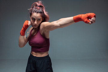 Beautiful female fighter trains in boxing bandages in studio isolateed on gray background. Mixed...