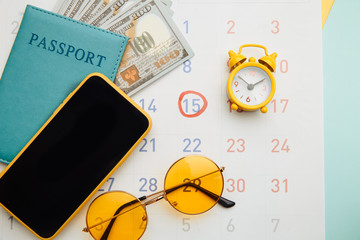 Calendar with passport, sunglasses and smartphone on blue background. Vacation planning concept.
