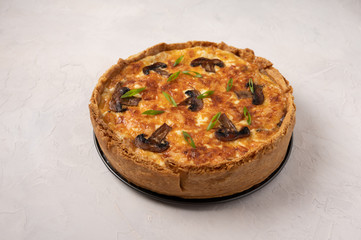 Traditional French pie quiche with mushrooms and cheese on a light textured background, close up, copy space