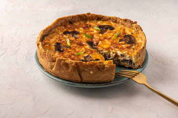 Traditional French pie quiche with mushrooms and cheese on a plate, next to a fork, on a light textured background, copy space, top view 