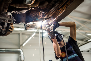 Car mechanic with protective mask welding car. Service station
