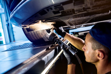 Car mechanic examining car suspension of lifted automobile at service station