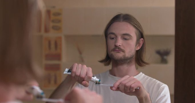 Young man looks in the mirror and squeezes the toothpaste onto the toothbrush