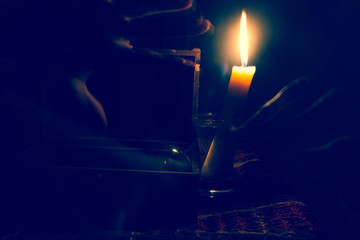 Performing magic rites, witchcraft. A candle illuminates the darkness.