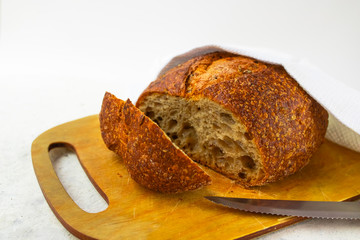 Freshly baked cereal bread on a wooden board under a white towel.