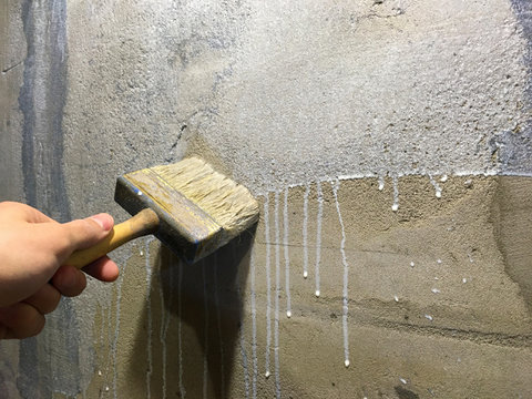 Primer process of concrete close up. Worker's hand in a glove with a brush primers a concrete wall