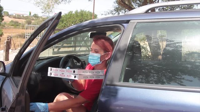 Female Pizza Delivery Boy Delivering Two Cartons Of Italian Pizza Directly To The Customer's Home, Getting Out Of The Car With A Health Mask Over His Mouth To Prevent The Covid19 Virus