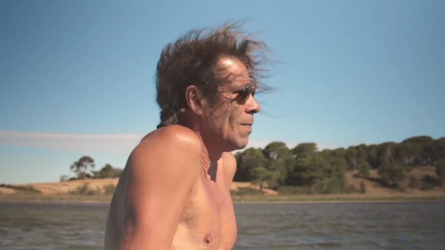 Un homme mature avec des lunettes de soleil contemple le paysage lagunaire assis sur une barque, plan rapproch&eacute;, il fait beau, l'encre est jet&eacute; la barque ondule.