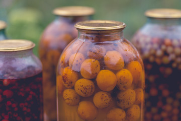 Close up of canned juice with fruits and berries. Sealed jars of compote on blurred background.