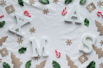 Creative Christmas flat lay with large white letters Xmas on white textile tablecloth. Wintertime zero waste craft paper decorations.