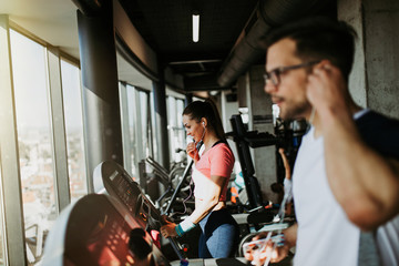 Young fit man and woman running on treadmill in modern fitness gym.