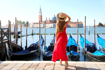 Fototapeta na wymiar Back view of beautiful girl in red dress walking in Venice with gondolas moored