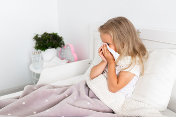 Toddler girl is lying in bed. The child is cold and sick and has a runny nose and snot. The child wipes his nose with a napkin. Allergy, flu.