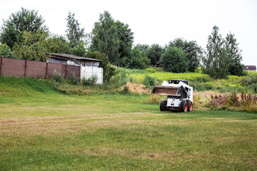 A skid steer loader clears the site for construction. Land work by the territory improvement. Machine for work in confined areas. Small tractor with a bucket for moving soil and bulk materials.
