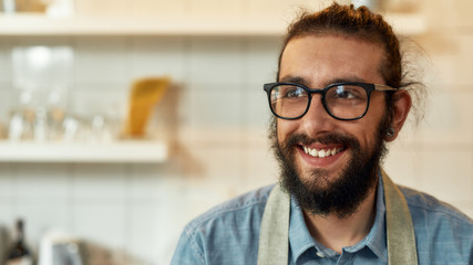 Close up portrait of young man, Italian cook in apron smiling aside, ready for preparing a meal in the kitchen. Cooking at home concept