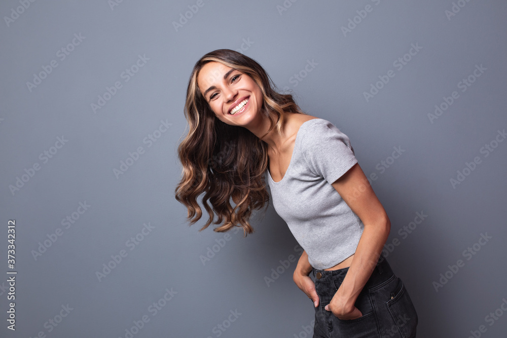 Wall mural Laughing young woman standing against a gray wall.