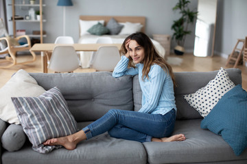 Relaxed smiling woman sitting on sofa at home.