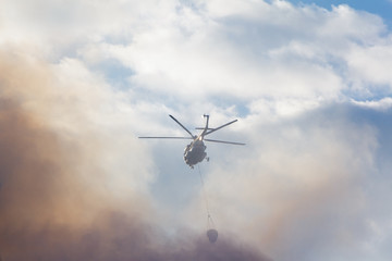 Fototapeta na wymiar Fire-fighting helicopter against the background of smoke and sky