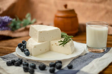 A glass of goat milk and a head of goat milk cheese stand on a wooden table. Cheese at home.