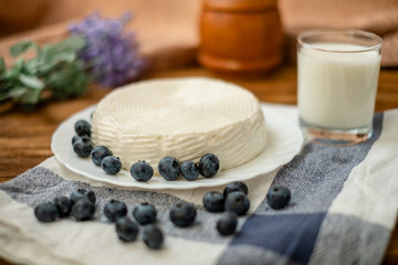 A glass of goat milk and a head of goat milk cheese stand on a wooden table. Cheese at home.