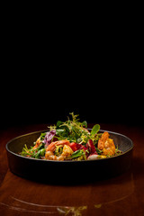Shrimps salad with cherry tomatoes, cucumeber, avocado, lettuce and pomegranate on dish. Healthy seafood concept. Tasty grilled prawn shrimp and mix vegetable salad on black wood